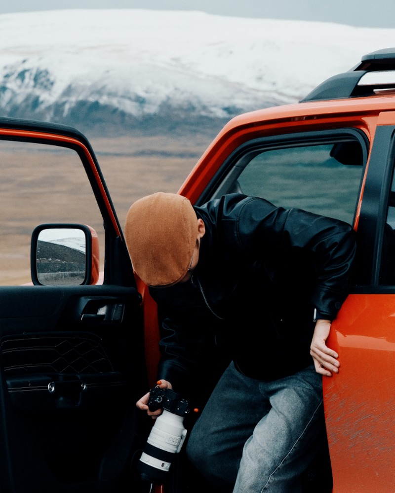 Hardy stepping out of an orange off-road vehicle with a camera in a snowy landscape
